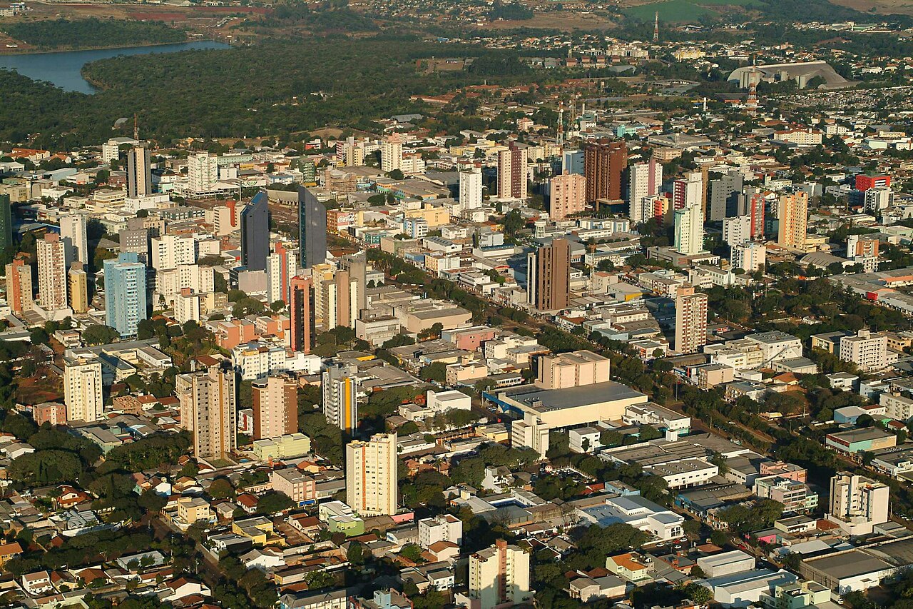 Vista aérea do centro de Cascavel, Paraná, com prédios, avenida arborizada e lago ao fundo